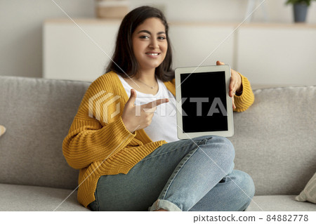 Internet purchases concept. Happy arab lady pointing at tablet screen with mockup for app or website design, copy space 84882778