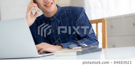 Young asian man talking phone and work from home with laptop computer. Young asian man talking phone and work from home with laptop computer. 84883021
