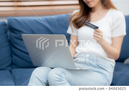 Young asian woman sit on sofa using laptop computer shopping online with credit card. 84883025