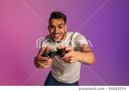 Handsome young Arab man using joystick, playing online video game in neon light Handsome young Arab man using joystick, playing online video game in neon light 84883034