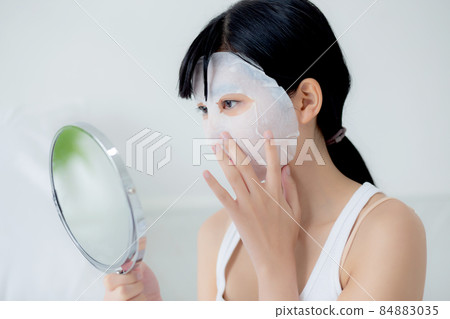 Beautiful young asian woman with sheet facial mask and looking mirror at home. Beautiful young asian woman with sheet facial mask and looking mirror at home. 84883035