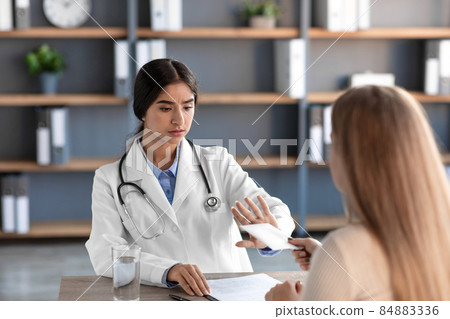 Shocked young indian lady doctor in white coat with stethoscope refuses of patient money Shocked young indian lady doctor in white coat with stethoscope refuses of patient money 84883336