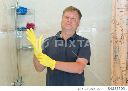 A man puts rubber gloves on his hand for cleaning the bathroom A man puts rubber gloves on his hand for cleaning the bathroom 84883503