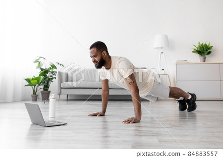 Attractive serious young african american man with beard in white sportswear in minimalist living room Attractive serious young african american man with beard in white sportswear in minimalist living room 84883557