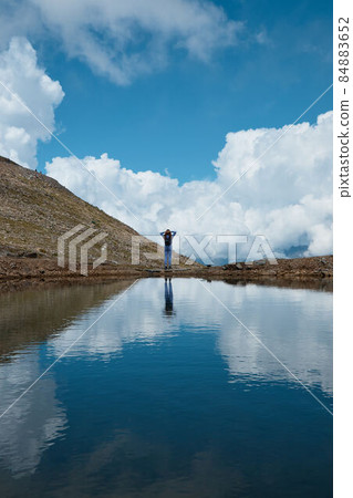 a girl on the edge of a lake, a mountain lake from a glacier, a shadow and a blue sky, a reflection in the water of clouds 84883652