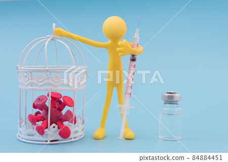 An optimistic yellow man holds a cage with coronavirus in his hands. The concept of defeating a pandemic with vaccination or medication. In the other hand, the man has a syringe. There's a vaccine 84884451