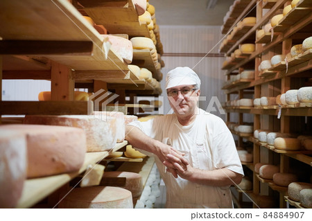 Cheese maker at the storage with shelves full of cow and goat cheese Cheese maker at the storage with shelves full of cow and goat cheese 84884907