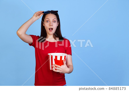 Half-length portrait of excited young girl in red t-shirt watching 3D movie isolated on blue studio background. Concept of emotions 84885173