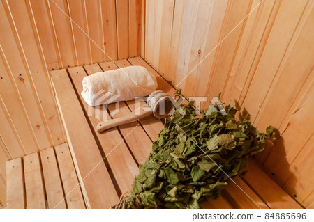 Traditional old Russian bathhouse SPA Concept. Interior details Finnish sauna steam room with traditional sauna accessories set towel birch broom scoop felt. Relax country village bath concept Traditional old Russian bathhouse SPA Concept. Interior details Finnish sauna steam room with traditional sauna accessories set towel birch broom scoop felt. Relax country village bath concept 84885696