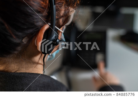 A woman call center operator in a medical mask answers the phone. A woman call center operator in a medical mask answers the phone. 84885776