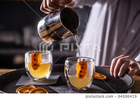 The bartender in the pub or restaurant prepares and pours the HOT TODDY winter drink into glass cups The bartender in the pub or restaurant prepares and pours the HOT TODDY winter drink into glass cups 84886419