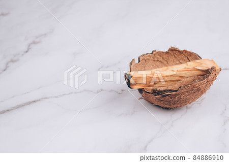 Burning Palo Santo tree sticks inside coconut shell on light marble table background - holy incense tree from Latin America. Meditation, mental health and personal fulfilment concept. Selective focus 84886910