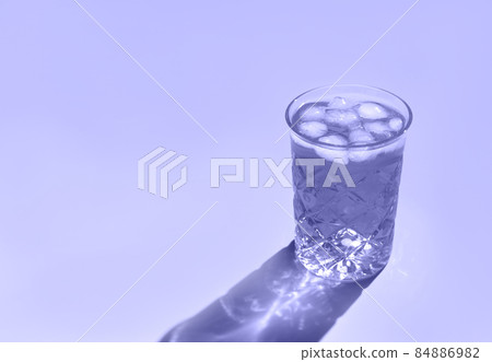 Beautiful crystal glass casts long shadow from sunlight. Toned in trendy color of year 2022. Minimal creative composition with copy space. Summer drinks concept. 84886982