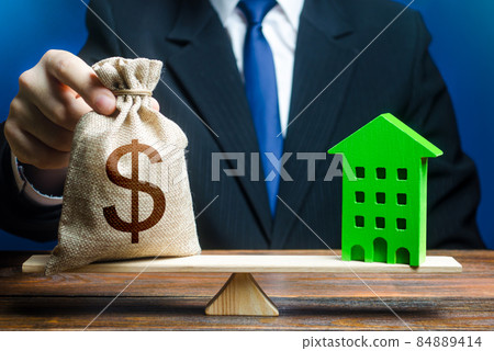 Businessman puts dollar money bag on scales and green house. Profitability housing of eco technologies. Investment in renovation. Reduced CO2 emissions, energy efficiency. Payback period 84889414