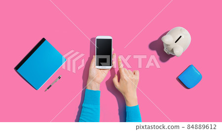 Person using smartphone with piggy bank Person using smartphone with piggy bank 84889612