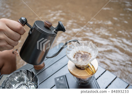Man dripping hot coffee and camping near river at nature park. Outdoor activity and relax on holiday. Man dripping hot coffee and camping near river at nature park. Outdoor activity and relax on holiday. 84893233