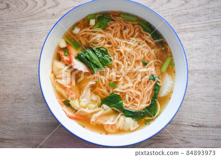 soup noodle wonton pork yellow noodle with red roasted pork dumpling and bog choy chinese vegetable in soup bowl on wooden table, top view 84893973