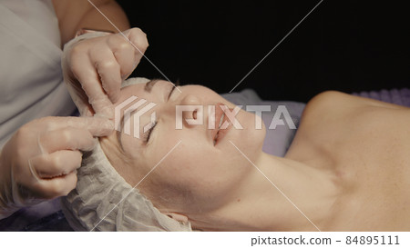 Woman receiving anti-ageing facial massage in spa salon relax. Wellness body skin care face beauty treatment. Black background 84895111