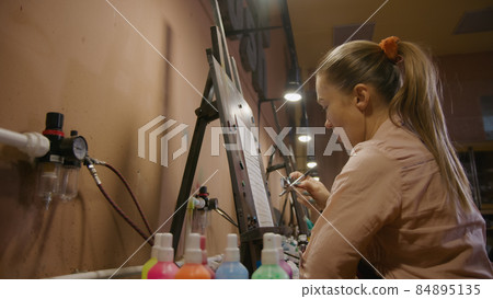Woman artist learns to paint with airbrush with acrylic dye, paper and easel. Concept modern art, airbrushing, aerography, graffiti, aerosol spray 84895135