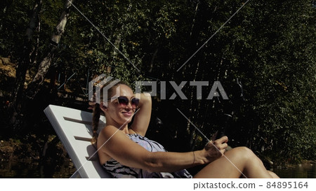 Woman shooting on handheld film gimbal stabilization for smartphone. Girl lie sunbed on pier make selfie. Blogger broadcast video vlogging. Woman shooting on handheld film gimbal stabilization for smartphone. Girl lie sunbed on pier make selfie. Blogger broadcast video vlogging. 84895164
