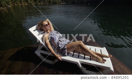 Woman lie on a sunbed in sunglasses and a boho silk shawl. Girl rest on a flood wood underwater pier. The pavement is covered with water in the lake. Woman lie on a sunbed in sunglasses and a boho silk shawl. Girl rest on a flood wood underwater pier. The pavement is covered with water in the lake. 84895201