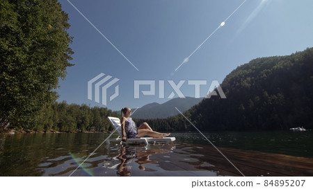 Woman lie on a sunbed in sunglasses and a boho silk shawl. Girl rest on a flood wood underwater pier. The pavement is covered with water in the lake. Woman lie on a sunbed in sunglasses and a boho silk shawl. Girl rest on a flood wood underwater pier. The pavement is covered with water in the lake. 84895207