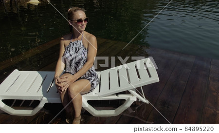 Woman lie on a sunbed in sunglasses and a boho silk shawl. Girl rest on a flood wood underwater pier. The pavement is covered with water in the lake. Woman lie on a sunbed in sunglasses and a boho silk shawl. Girl rest on a flood wood underwater pier. The pavement is covered with water in the lake. 84895220