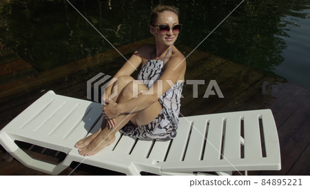 Woman lie on a sunbed in sunglasses and a boho silk shawl. Girl rest on a flood wood underwater pier. The pavement is covered with water in the lake. Woman lie on a sunbed in sunglasses and a boho silk shawl. Girl rest on a flood wood underwater pier. The pavement is covered with water in the lake. 84895221