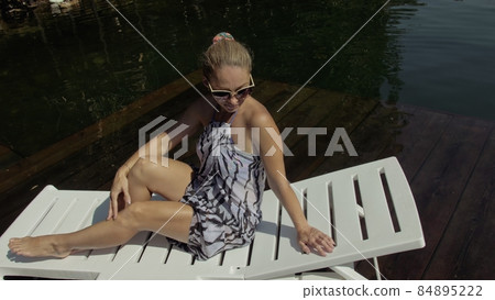 Woman lie on a sunbed in sunglasses and a boho silk shawl. Girl rest on a flood wood underwater pier. The pavement is covered with water in the lake. Woman lie on a sunbed in sunglasses and a boho silk shawl. Girl rest on a flood wood underwater pier. The pavement is covered with water in the lake. 84895222