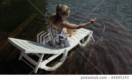 Woman lie on a sunbed in sunglasses and a boho silk shawl. Girl rest on a flood wood underwater pier. The pavement is covered with water in the lake. Woman lie on a sunbed in sunglasses and a boho silk shawl. Girl rest on a flood wood underwater pier. The pavement is covered with water in the lake. 84895243
