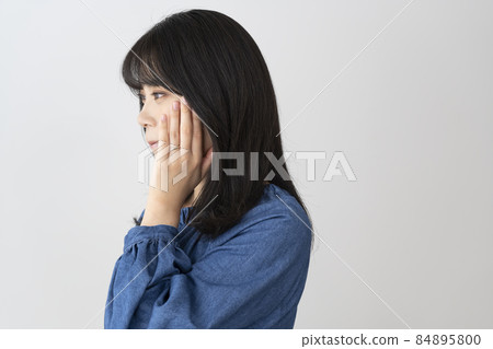 A young woman wearing a wedding ring and putting her hand on her cheek 84895800