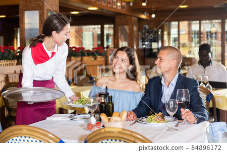 Diligent female waiter bringing order to visitors in restaurant 84896172