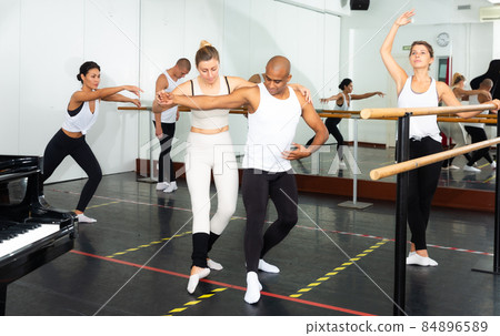 Ballet teacher adjusting foot positions in class 84896589