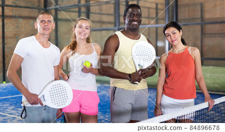 Four smiling men and women with padel rackets posing at court 84896678
