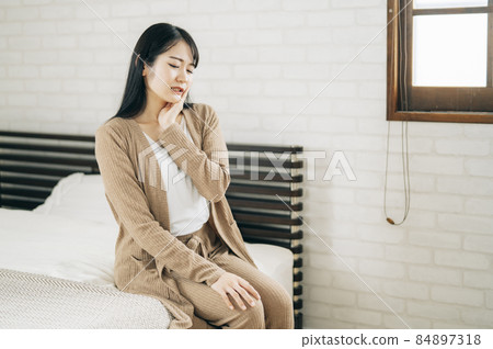 A Japanese woman sitting on the bed and suffering from tooth decay, periodontal disease, and herpes 84897318