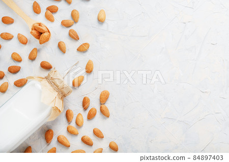 Almond milk in a glass bottle on a light background with a scattering of seed kernels and a wooden spoon. Almond milk in a glass bottle on a light background with a scattering of seed kernels and a wooden spoon. 84897403
