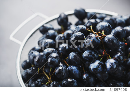 Sweet black grapes in a metal bowl on a dark textured background. 84897408