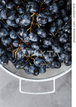 Sweet black grapes in a metal bowl on a dark textured background. 84897409