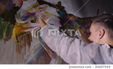 Artist designer draws an eagle on the wall. Craftsman decorator paints picture with acrylic oil color. Painter painter dressed in paint coat. Indoor. Artist designer draws an eagle on the wall. Craftsman decorator paints picture with acrylic oil color. Painter painter dressed in paint coat. Indoor. 84897444
