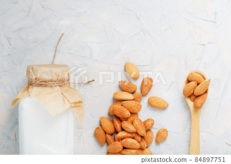 Almond milk in a bottle with a handful of seeds and a wooden spoon on a light background. 84897751
