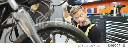 Surprised male repairman scratching his head with spanner and looking at motorcycle 84900648