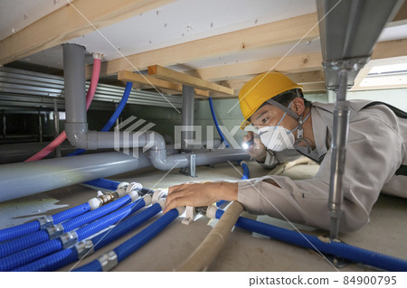 一個穿著工作服的男人在檢查房子地板下的水管 一個穿著工作服的男人在檢查房子地板下的水管 84900795