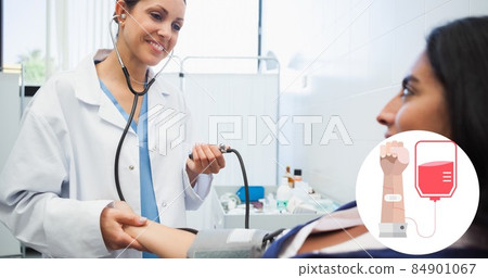 Smiling doctor checking blood pressure of female patient at hospital with blood donation symbol 84901067
