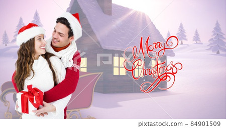 Happy couple in santa hats holding gift by christmas greeting while snow covered house in background Happy couple in santa hats holding gift by christmas greeting while snow covered house in background 84901509