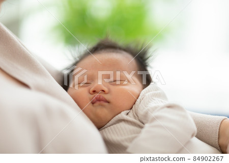 Adorable sleeping newborn baby relax in mother arm safety and comfortable.Smile Asian newborn infant baby resting sleeping sweet dream.Mother holding infant baby.Newborn Baby photography concept Adorable sleeping newborn baby relax in mother arm safety and comfortable.Smile Asian newborn infant baby resting sleeping sweet dream.Mother holding infant baby.Newborn Baby photography concept 84902267