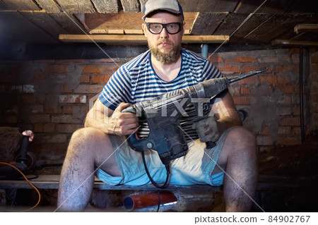 Funny bearded man with heavy duty perforator in the basement of the house Funny bearded man with heavy duty perforator in the basement of the house 84902767