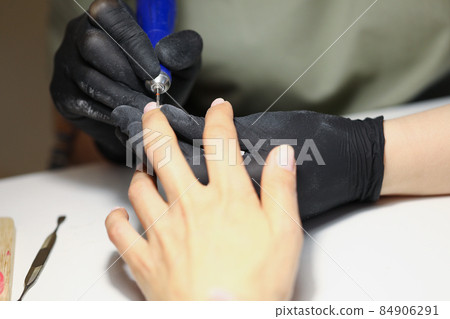 Nail master using electrical equipment to clean client nails in modern beauty studio Nail master using electrical equipment to clean client nails in modern beauty studio 84906291
