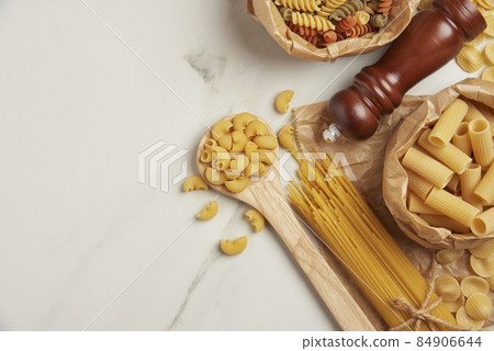 pasta concept some types of pasta being organized on wooden spoons and in paper bags while some and other ingredients being put on white background pasta concept some types of pasta being organized on wooden spoons and in paper bags while some and other ingredients being put on white background 84906644