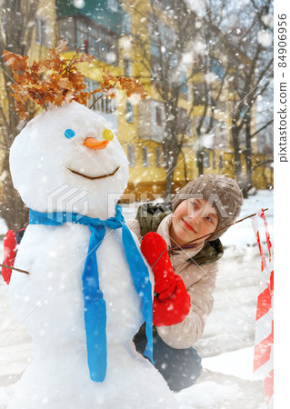 a girl plays with snow on a city street and makes a snowman 84906956