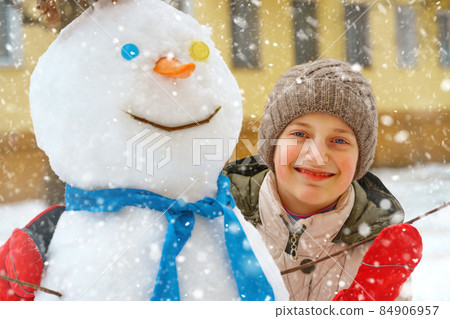 a girl plays with snow on a city street and makes a snowman 84906957